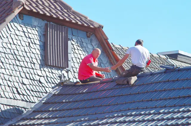 Two roofers working on a house roof